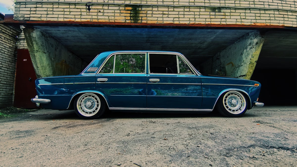 Retro blue Zhiguli sedan parked by a rustic brick building, showcasing vintage charm.